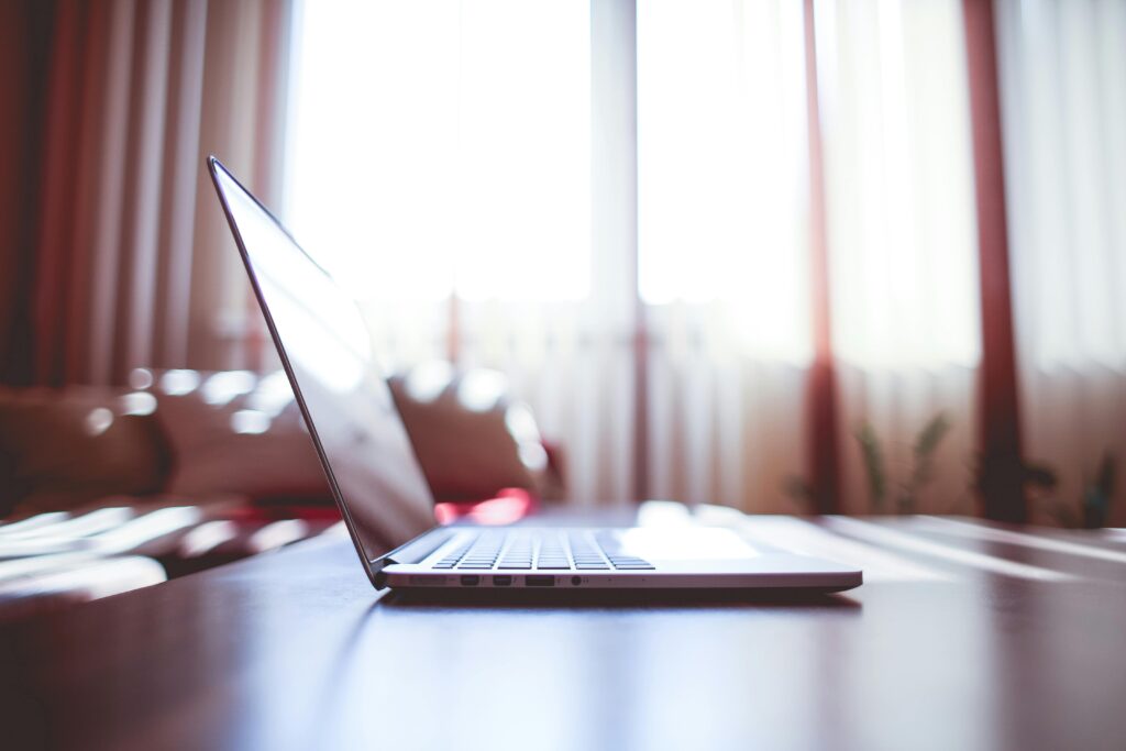 A modern laptop on a table illuminated by soft natural light from nearby windows.